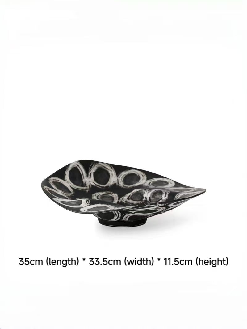 abstract black and white ceramic bowl with organic wavy edges and hand-painted circular patterns on a white console.