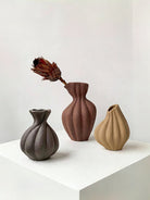 artisan biomorphic ceramic vases with twisted ridge textures, earthy terracotta and basalt grey sculptural pottery on a white surface.