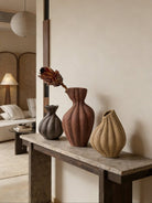 artisan biomorphic ceramic vases with twisted ridge textures, earthy terracotta and basalt grey sculptural pottery on a white surface.