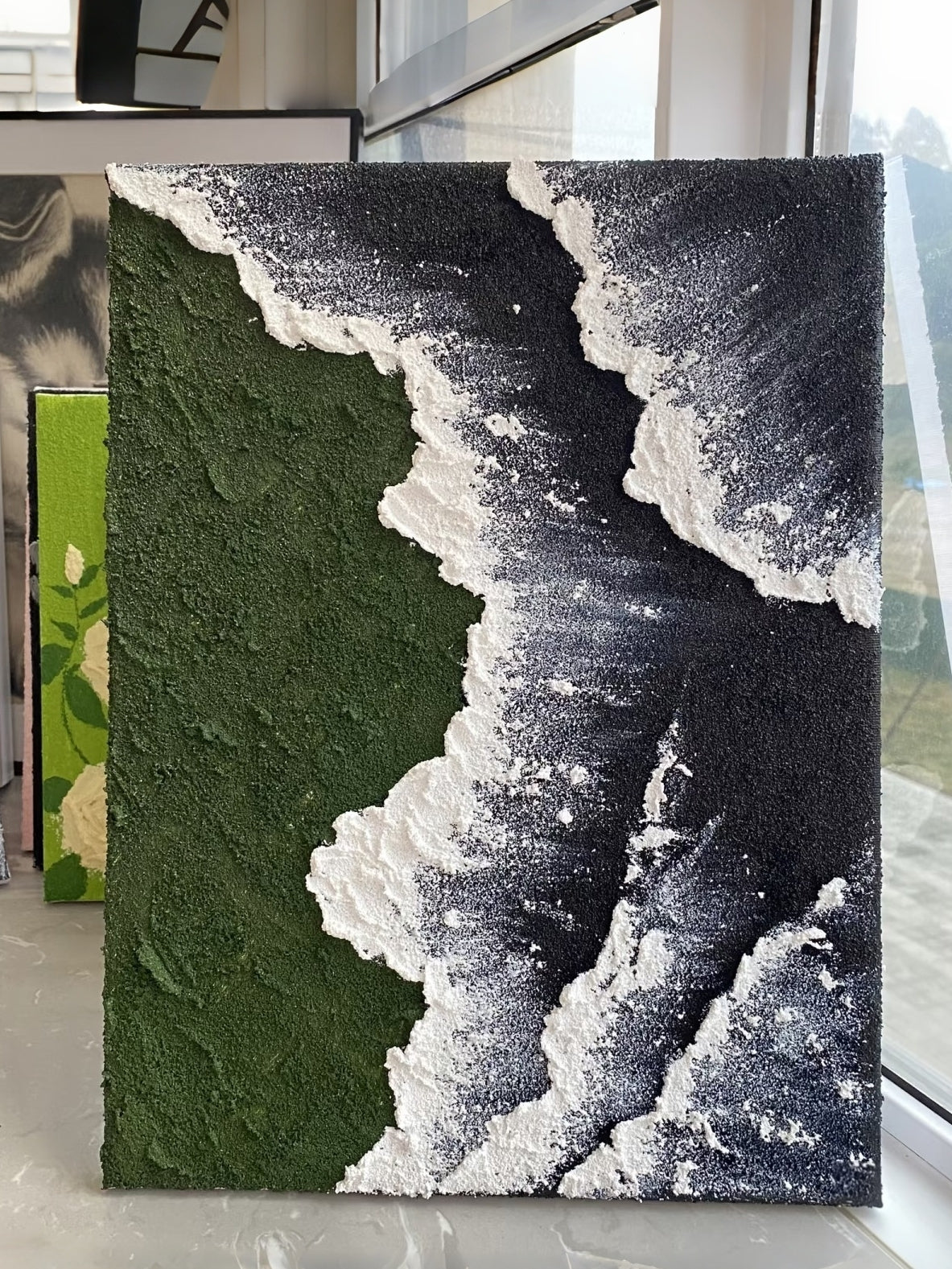 Close-up of a hand-painted 3D textured abstract painting featuring heavy white sculpted foam over moss green and black backgrounds in a gold frame.