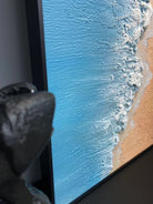 Hand-painted 3D textured aerial view of beach waves with heavy white sculpted foam and granular golden sand texture in a gold frame.