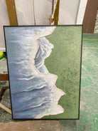 Side view of 3D hand-painted textured painting showing thick white seafoam between moss green meadow and slate blue ocean.