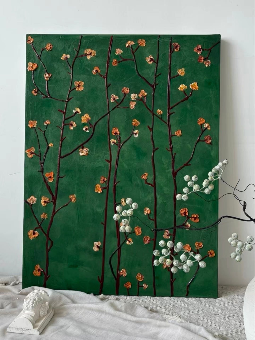 Close-up of heavy textured hand-painted floral oil painting with emerald green background and amber flower blossoms on dark branches.