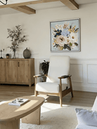 Large square 3D textured floral painting showing heavy impasto pink and white flowers on a light blue background in a modern living room.