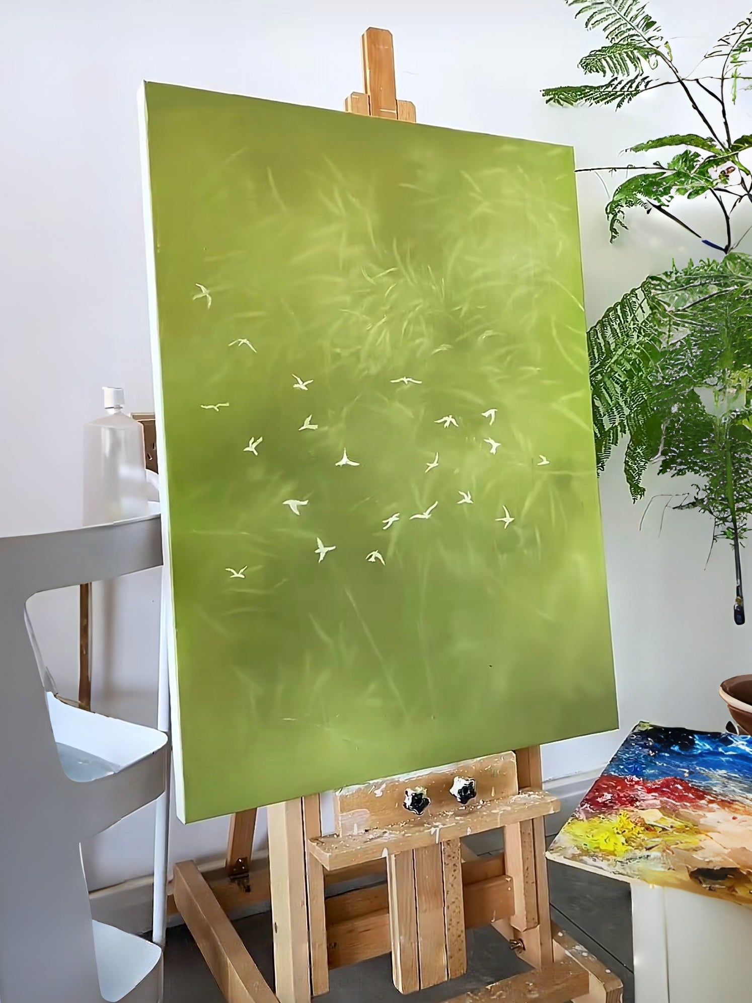 Large vertical hand-painted abstract forest painting in sage green with white flying birds by Luna Xiao in a modern neutral bedroom.