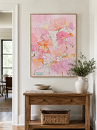 Blush floral wall art above a wood console in a bright entryway