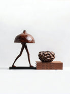 surrealist walking mushroom sculpture in bronze brown resin, paired with textured geometric vases on a bookshelf for modern home decor.
