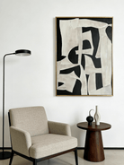 Large vertical hand-painted abstract painting with bold black and white geometric shapes and heavy impasto texture by Seraphina Rose in a modern luxury living room.